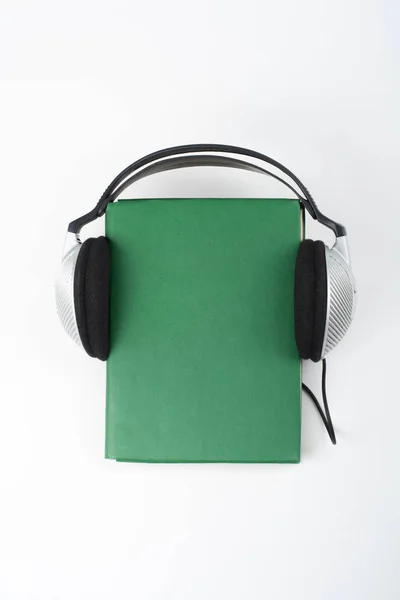 白い背景のオーディオ ブック 緑のハードカバー本 空のカバーに入れてヘッドフォンは 広告テキストのためのスペースをコピーします 遠隔教育 ラーニングの概念 — ストック写真