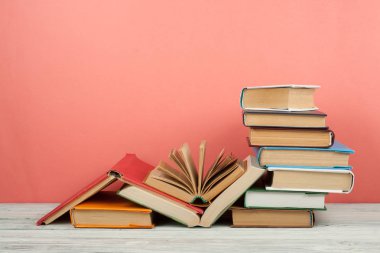 Kitap istifleme. Açık bir kitap, ahşap masa ve pembe arka plan üzerine ciltli kitaplar. Okula dönelim. Metin için alanı kopyala.
