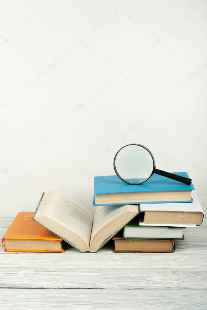 Open book, hardback colorful books on wooden table. Magnifier. Back to school. Copy space for text. Education business concept