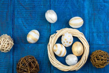 Mutlu Paskalyalar. Tahta masa arkasında izole edilmiş yumurtalar... Toplar, sarmaşıklardan örülmüş çelenkler. Uzayı metin için kopyala. Üst görünüm