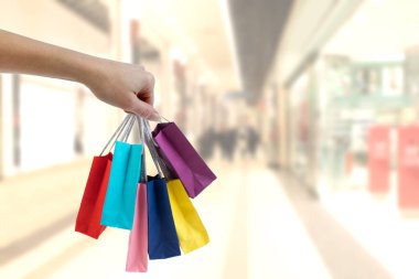Alışveriş merkezi arka plan üzerinde renkli kağıt torba tutarak kırpma el.