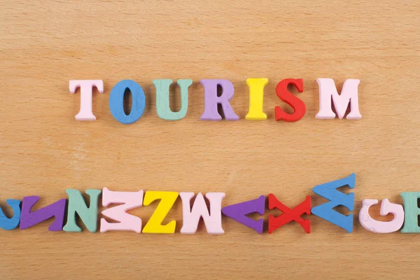 Tourismus-Wort auf hölzernem Hintergrund, bestehend aus bunten Abc-Buchstaben-Block-Holzbuchstaben, Kopierfläche für Anzeigentext. Englischlerndes Konzept. — Stockfoto