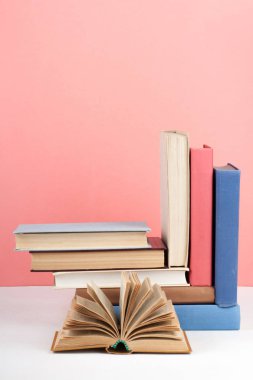 Açık kitap, ahşap masa üzerinde ciltli renkli kitaplar, kırmızı, pembe arka plan. Okula geri dön. Metin için alan kopyalayın. Eğitim iş kavramı.