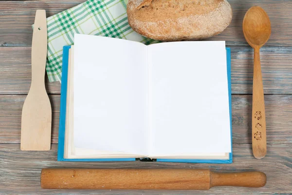 Відкрита книга рецептів на дерев'яному фоні, ложці, штифті, зеленій картатій скатертині . — стокове фото
