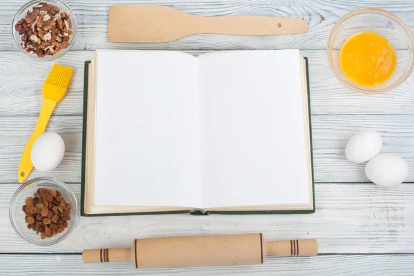 Recipe cook blank book on wooden background, spoon, rolling pin, checkered tablecloth. Top view