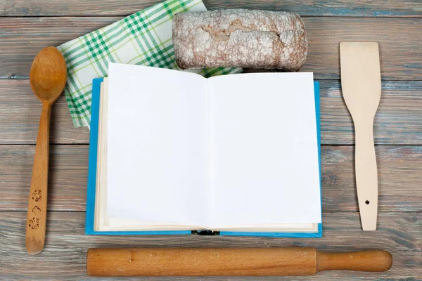 Libro de recetas abierto sobre fondo de madera, cuchara, rodillo, mantel a cuadros verde . — Foto de Stock