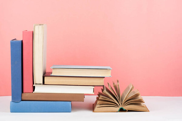 Book stacking. Open book, hardback books on wooden table and pink background. Back to school. Copy space for text