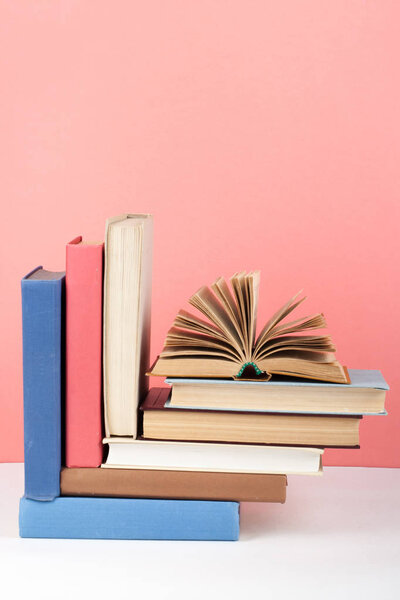 Open book, hardback colorful books on wooden table, red, pink background. Back to school. Copy space for text. Education business concept.