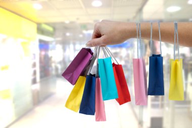 Alışveriş merkezi arka plan üzerinde renkli kağıt torba tutarak kırpma el.