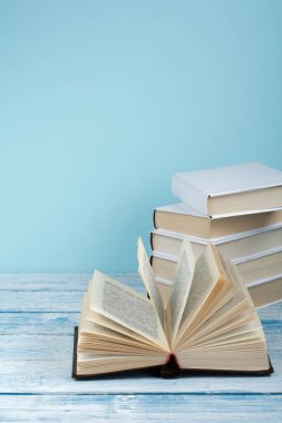 Kitap istifleme. Açık kitap, ahşap masa ve mavi arka plan üzerine ciltli kitaplar. Okula dönelim. Metin için alanı kopyala.