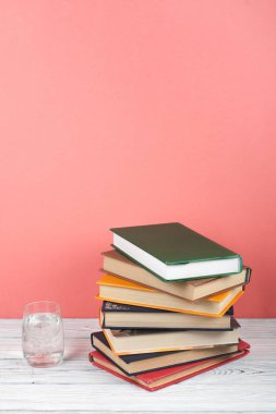 Kitap istifleme. Açık bir kitap, ahşap masa ve pembe arka plan üzerine ciltli kitaplar. Okula dönelim. Metin için alanı kopyala.