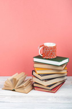 Kitap istifleme. Açık bir kitap, ahşap masa ve pembe arka plan üzerine ciltli kitaplar. Okula dönelim. Metin için alanı kopyala.