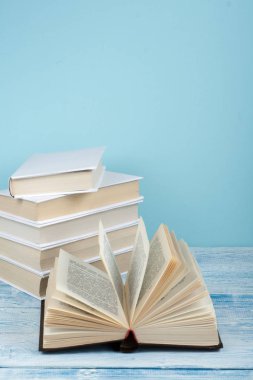 Kitap istifleme. Açık kitap, ahşap masa ve mavi arka plan üzerine ciltli kitaplar. Okula dönelim. Metin için alanı kopyala.