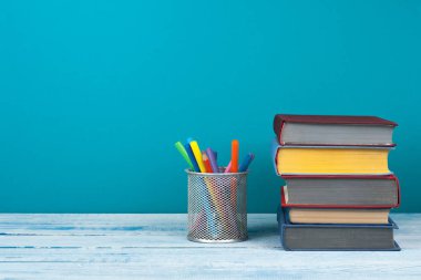 Kitap istifleme. Açık kitap, ahşap masa ve mavi arka plan üzerine ciltli kitaplar. Okula dönelim. Metin için alanı kopyala.