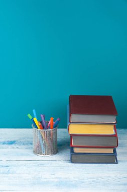 Kitap istifleme. Açık kitap, ahşap masa ve mavi arka plan üzerine ciltli kitaplar. Okula dönelim. Metin için alanı kopyala.