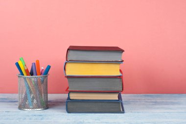 Kitap istifleme. Açık bir kitap, ahşap masa üzerinde ciltli kitaplar ve kırmızı, pembe arka plan. Okula dönelim. Metin için alanı kopyala