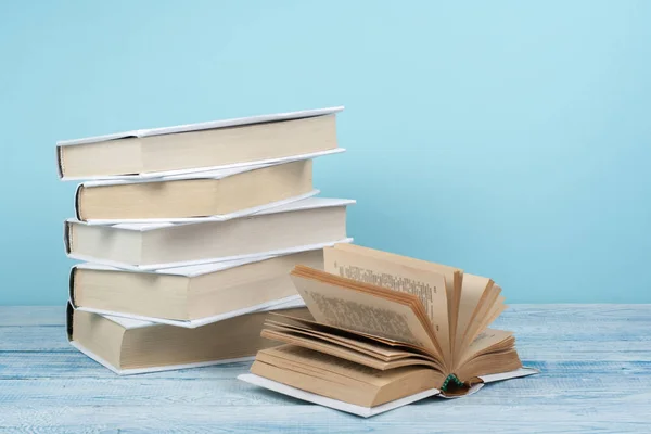 Apilamiento de libros. Libro abierto, libros de tapa dura sobre mesa de madera y fondo azul. De vuelta a la escuela. Copiar espacio para texto. —  Fotos de Stock