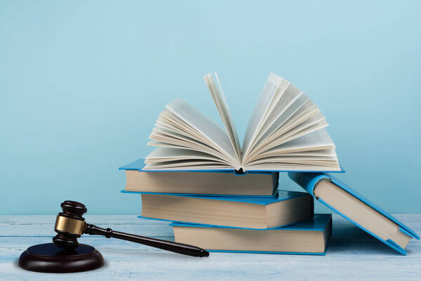 Law concept open book with wooden judges gavel on table in a courtroom or law enforcement office, blue background. Copy space for text.