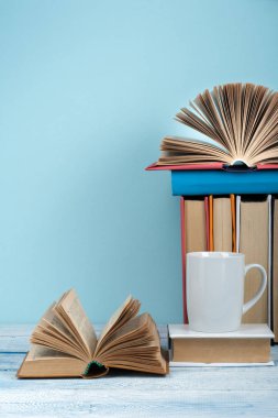 Açık kitap, ahşap masa ve mavi arka plan üzerine ciltli kitaplar. Okula dönelim. Metin için alanı kopyala.