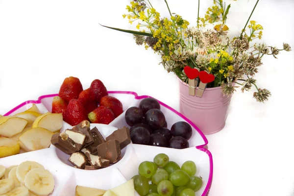 Fruit plate on a white background. Fruit and chocolate. Strawberry, banana, chocolate, grapes, apple, pear.