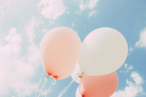 White pink balloons against the sky. Sunny weather and sky with clouds