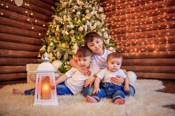 人の幸せな子供 ティーンエイ ジャーの男の子 幼児の女の子と自分の生まれたばかりの赤ちゃんの弟 美しいクリスマス ツリーの下で一緒に遊んで 男の子はクリスマス ツリーの下に座っています — ストック写真