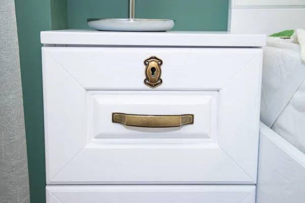 Dark handle on the white facade of the cabinet. Furniture fittings. Open and close the cabinet.