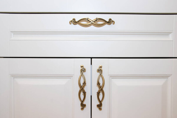 Dark handle on the white facade of the cabinet. Furniture fittings. Open and close the cabinet.