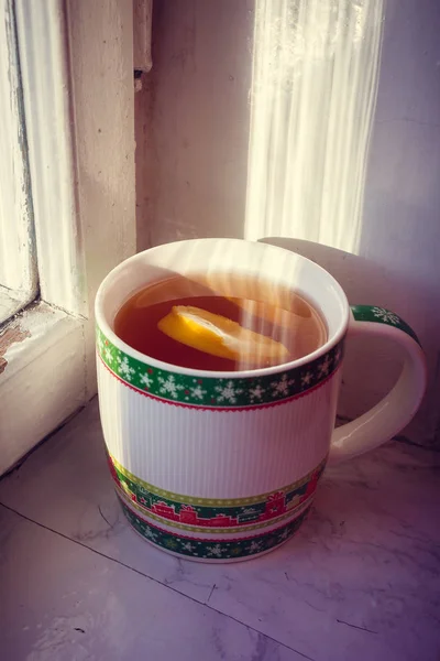 close up of cup with tea and lemon on window sill