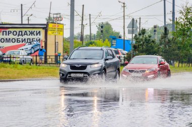 Arabadan yola su sıçratıyor. Yaz yağmuru. Yolda su birikintileri var. Rus yolları. Isliyiz sokağı. Su sıçratıyor. Rusya, Leningrad bölgesi Gatchina 21 Temmuz 2018