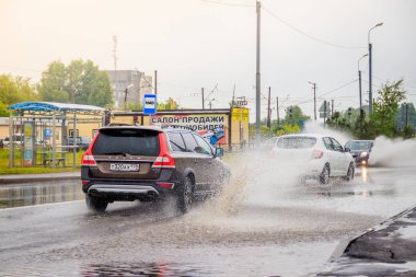 Arabadan yola su sıçratıyor. Yaz yağmuru. Yolda su birikintileri var. Rus yolları. Isliyiz sokağı. Su sıçratıyor. Rusya, Leningrad bölgesi Gatchina 21 Temmuz 2018