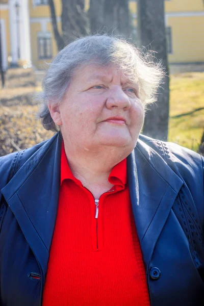 Uma idosa num banco da cidade. Avó em uma camisola vermelha e jaqueta de couro . — Fotografia de Stock