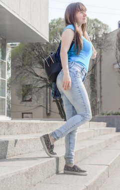 Kot pantolon ve T-Short giymiş genç ve güzel bir kadın sokakta merdivenlerde poz veriyor.