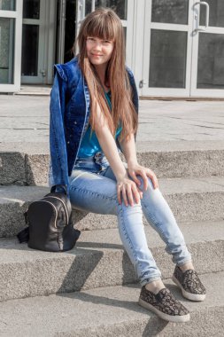 Kot pantolon ve T-Short giymiş genç ve güzel bir kadın sokakta merdivenlerde poz veriyor.