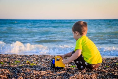 Küçük çocuk deniz arka planda renkli oyuncaklar ile çakıl plajda oynuyor 