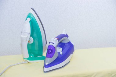 Ütü tahtasında iki ütü. Demirlerin seçimi ve karşılaştırılması. Ütü tahtası.