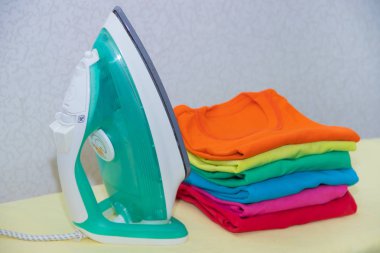 Demir ve bebek kıyafetleri. Ütü tahtasında renkli kıyafetler. Parlak tişörtler. Bir tahta üzerinde ütülenmiş renkli bebek iç çamaşırı. . Ütü tahtası. Bir yığın şey.