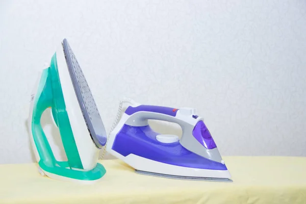 Two irons on an ironing board. Selection and comparison of irons. Ironing board.