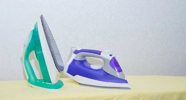 Two irons on an ironing board. Selection and comparison of irons. Ironing board.