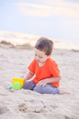 Küçük çocuk gündüz kumlu plajda plastik oyuncak araba ile oynuyor