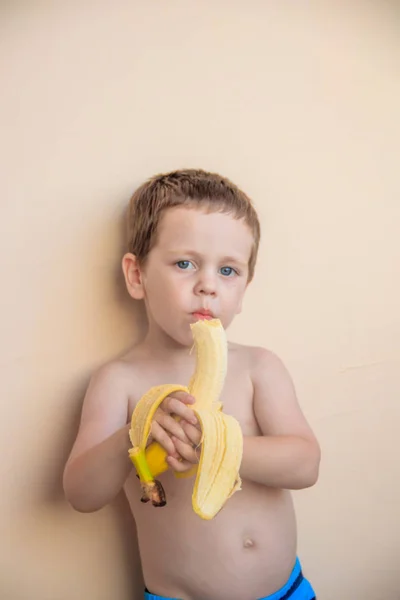 cute little boy eating banana on pastel background