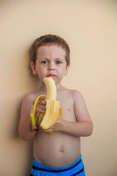cute little boy eating banana on pastel background