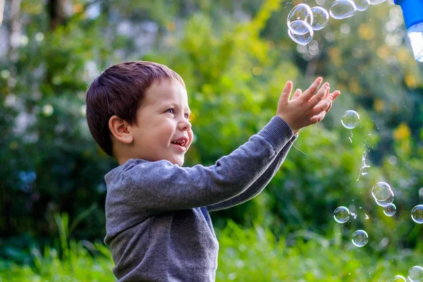 Ein Junge auf der Straße fängt Seifenblasen. glückliche Kindheit. Kinderspiele. — Stockfoto