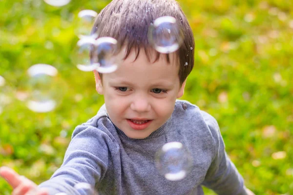 Um rapaz na rua apanha bolhas de sabão. Feliz infância. Jogos infantis . — Fotografia de Stock