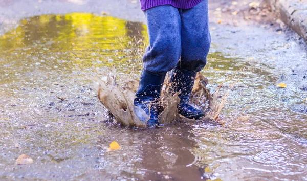 A little boy is jumping in a puddle. A boy in rubber boots. Happy childhood. Puddles after the rain. Warm summer evening. — Stock Photo, Image