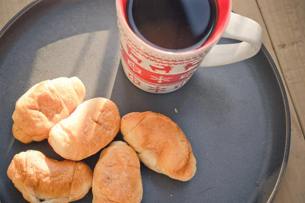 Café em uma xícara e croissants em uma chapa. Comida e bebidas. Placa em um fundo de madeira . — Fotografia de Stock