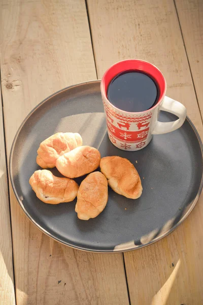 Café en una taza y cruasanes en un plato. Comida y bebidas. Placa sobre fondo de madera . — Foto de Stock