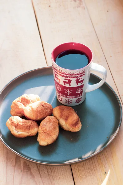 Café em uma xícara e croissants em uma chapa. Comida e bebidas. Placa em um fundo de madeira . — Fotografia de Stock