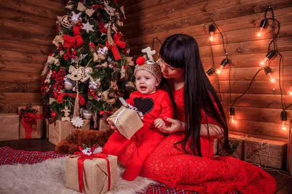 A mãe e o filho estão sentados debaixo da árvore de Ano Novo. Família de Natal. Férias de Ano Novo. Vestido até árvore de Natal . — Fotografia de Stock