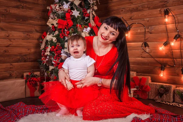 A mãe e a filha estão sentadas debaixo da árvore de Ano Novo. Família de Natal. Férias de Ano Novo. Vestido até árvore de Natal . — Fotografia de Stock